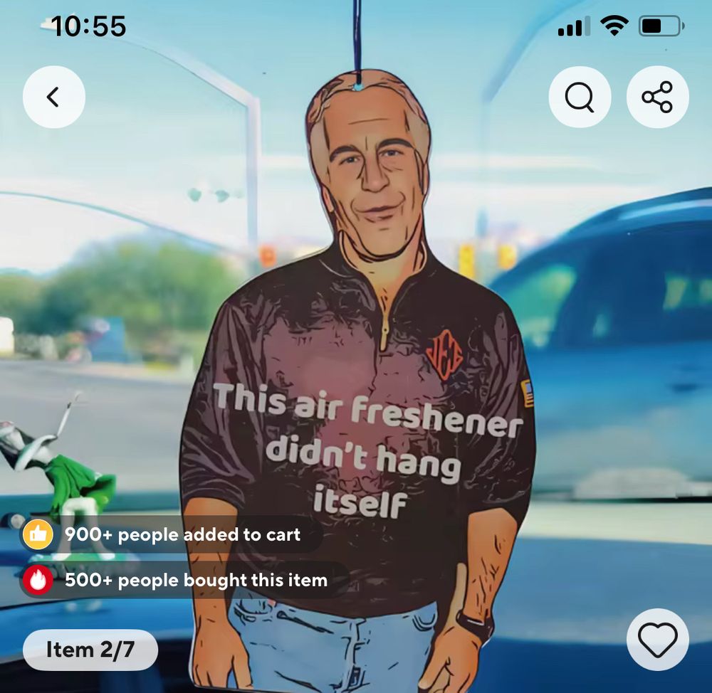 Product photo of a Jeffrey Epstein car air freshener hanging from a rear view mirror that says "This air freshener didn't hang itself" and what looks like an imminent head on collision with another car 
