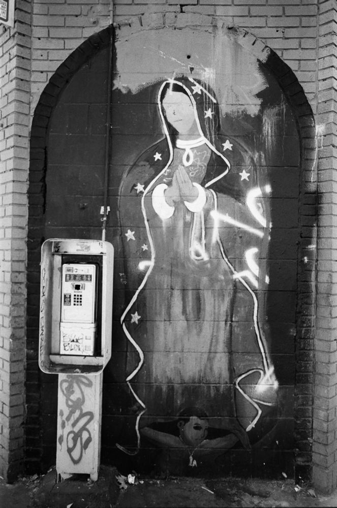 virgin mary guadalupe mural on a wall with a broken payphone