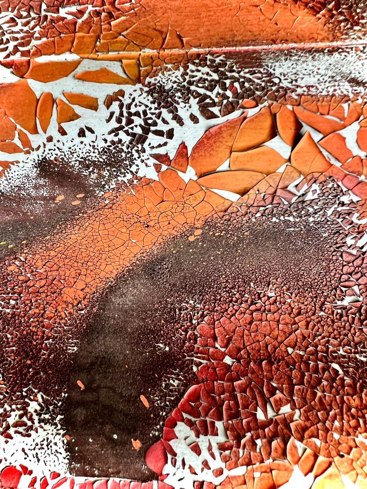 Photograph showing cracked paint on a metal sheet wall. Colors range from brown over yellow to orange.