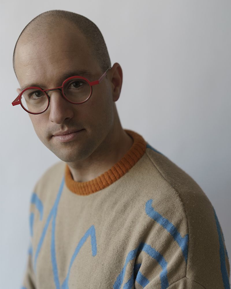 Constant Vigier looking at the camera. He's wearing glasses and a colorful jumper. It's a peaceful portrait.
