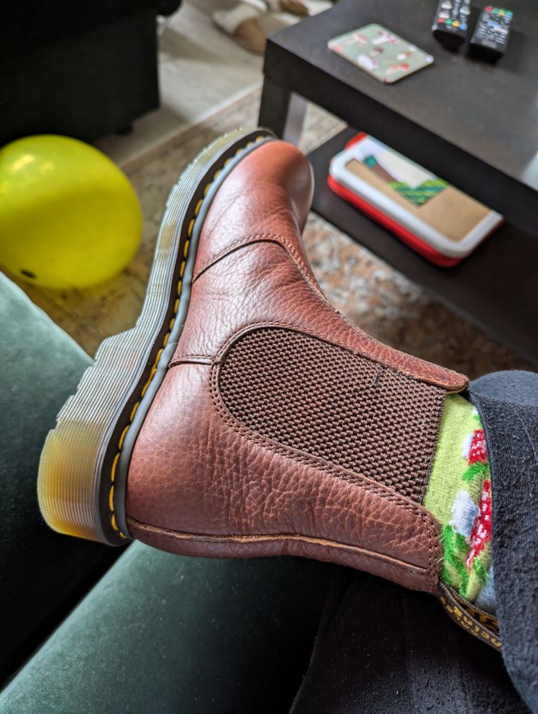 The side of a Dr. Martens boot, reddish brown in colour, on my foot. My green sock has red and white mushrooms on