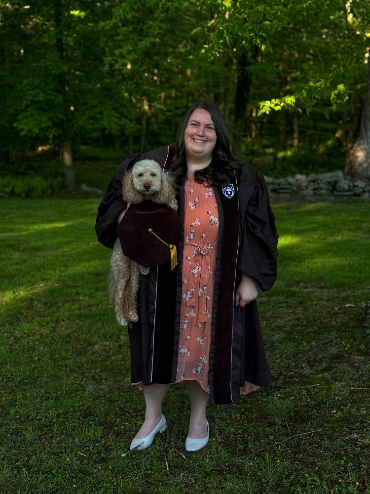 Photo of Kim in regalia holding a mini labradoodle