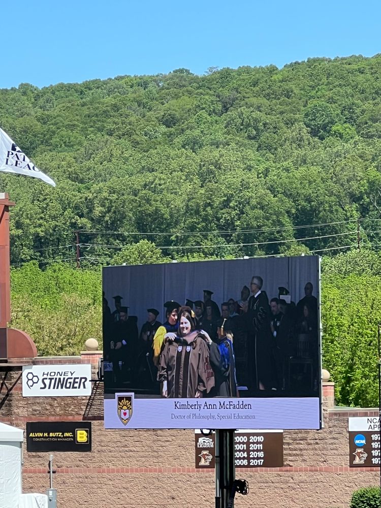 Photo of large screen at graduation showing Kim being hooded
