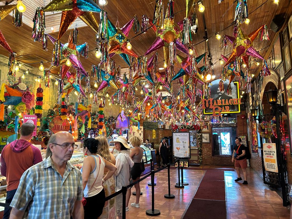 The interior lobby of Mi Tierra restaurant adorned with metallic piñatas. A row of guests line up to the left of the photo to order Mexican pastries.