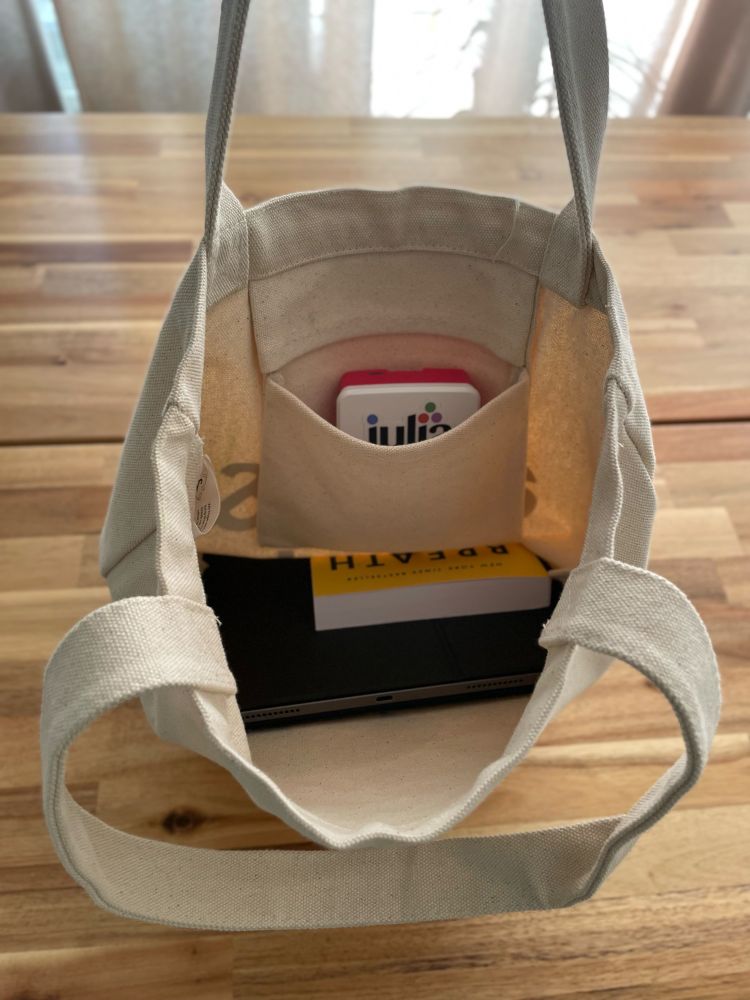 An open jute bag on wooden desk showing a raspberry pi minicomputer peaking outside of a small inside pocket.