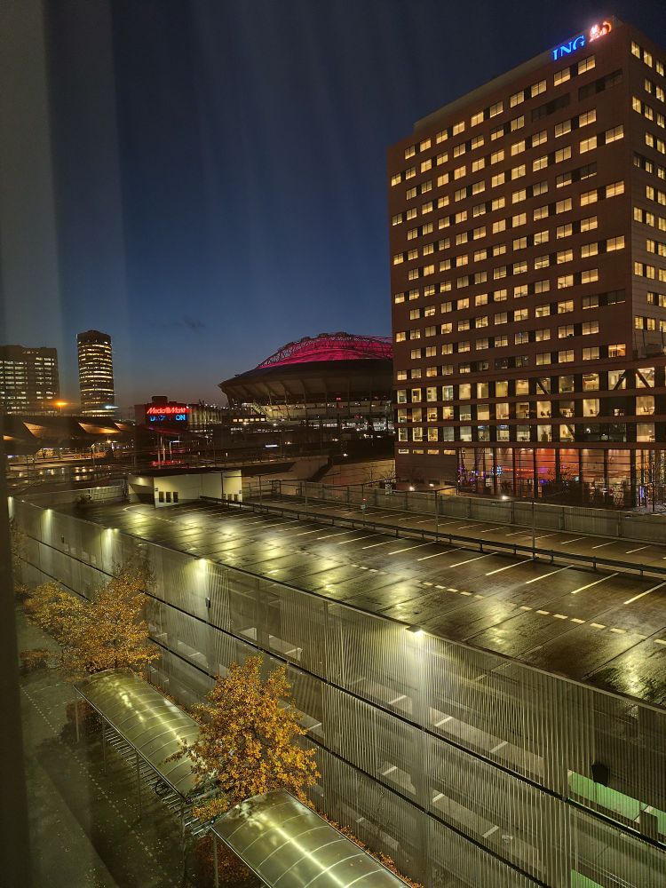 Uitzicht in het schemerdonker op een beetje rood verlichte Johan Cruijff Arena vanuit een hotelkamer.