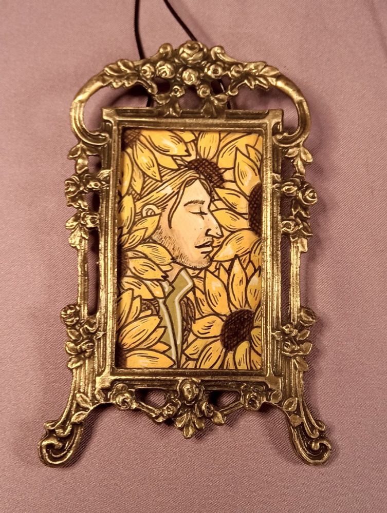 An acrylic painting of Anders, surrounded by sunflowers, in a little golden frame. 