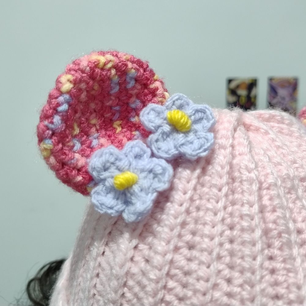 Touca rosa claro com orelhas de urso rosa escuro e aplique de flor lilás. Essa foto está com um zoom no detalhe da orelha