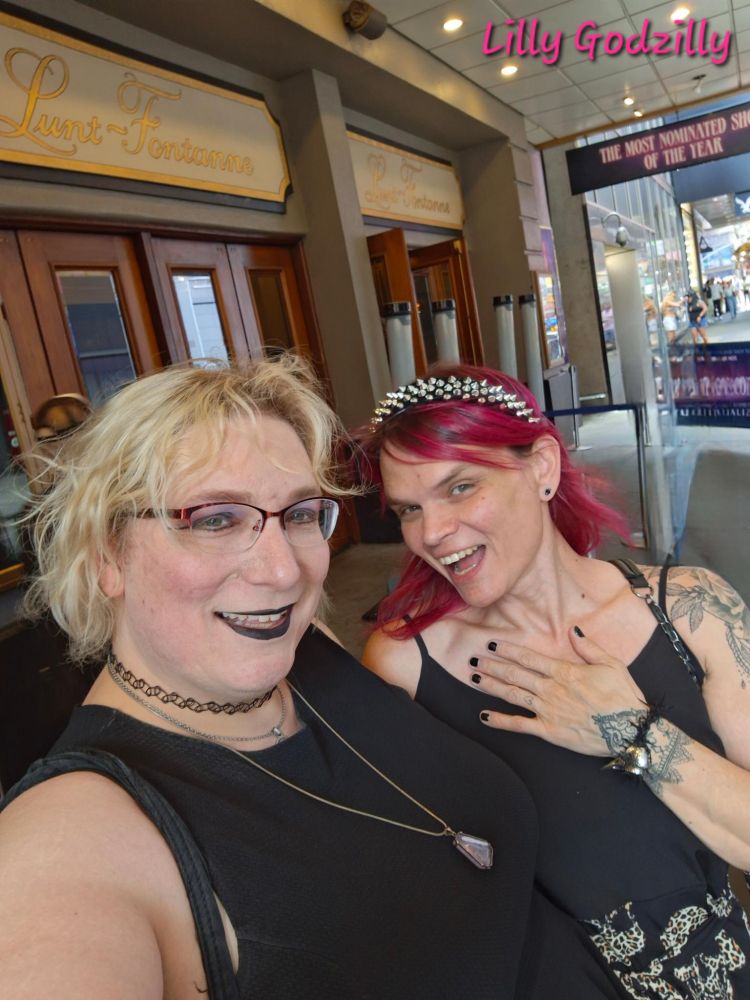 Lilly and Scotia are both wearing black dresses, lillys dress has skulls in lepoard pront on the skirts

 Scotia has blonde hair and Lilly has pink hair adorned with an amazing black headband with crome spikes all over it

Lilly and Scotia waiting in line outside of the theater 

