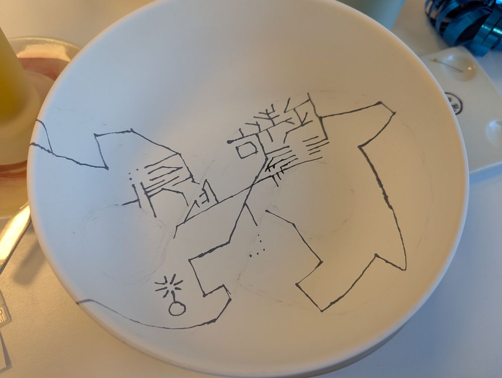 Ceramic bowl with a few black lines on it. There is one long line that seems to connect everything. Several smaller lines that go in different directions. 