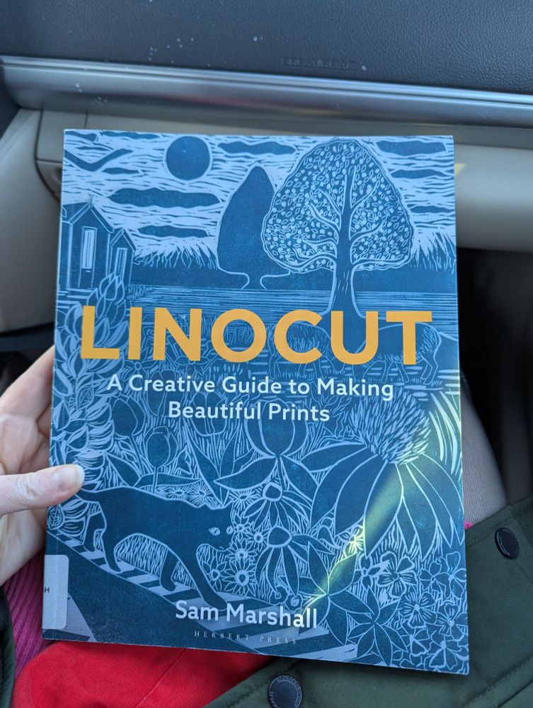 A hand holds a print book titled "Linocuts: A creative guide to making beautiful prints". The author is Sam Marshall.