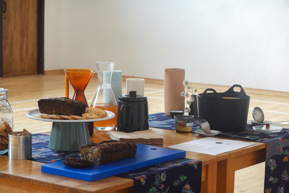 two tables with blue printed cloths hosting banana bread, shortbread cookies, selection of tea, kombucha, and fig jelly.