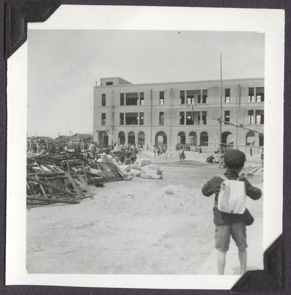 A child with their back turned to the camera looks at a pile of debris outside a building damaged in the bombing of Hiroshima, circa April 1947.