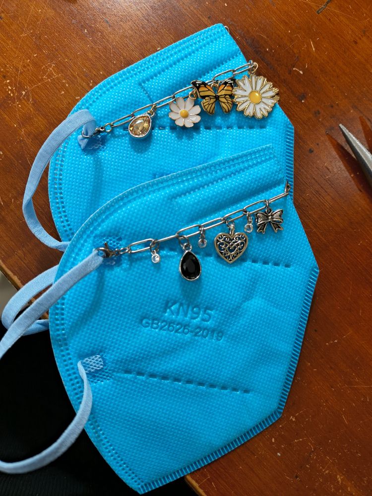 Two kn95 masks with chains on each - one with flower/butterflies and the other with hearts/bows