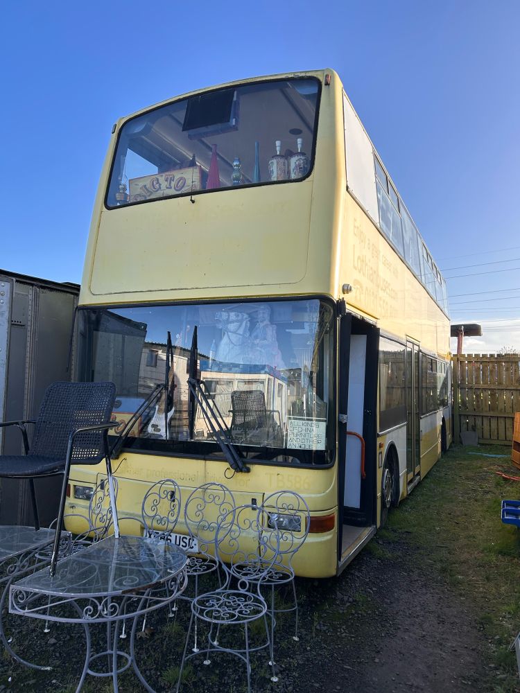 A decommisioned yellow double decker bus with a patio table and chairs outside. 