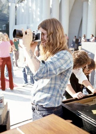 Foto a Ozzy Osbourne che guarda dentro il mirino di una macchina fotografica durante delle prove, così sembra da altre foto nella stessa serie, si vedono persone dietro, compreso Tommy Iommi.