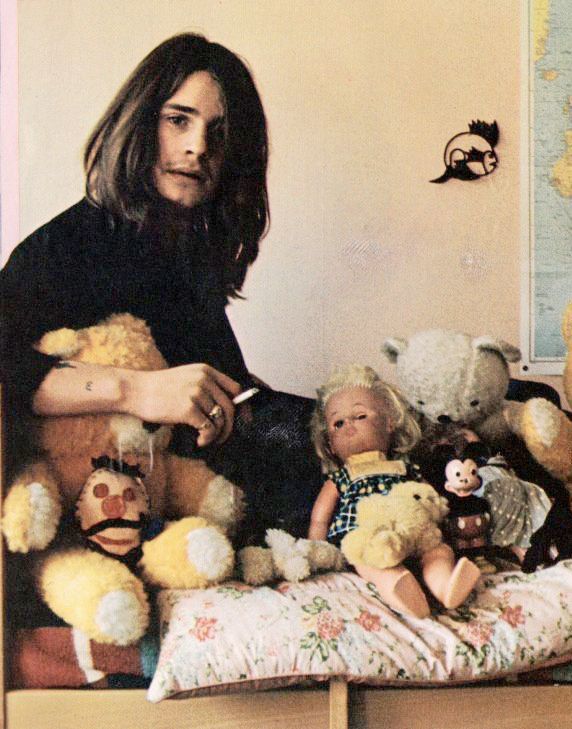 Ozzy Osbourne con sigaretta in mano seduto su un letto pieno di bambole e orsacchiotti