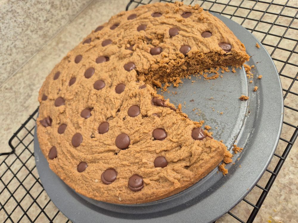 Cookiebde baunilha com gotas de chocolate, tamanho grande, em cima da forma e com uma fatia já cortada 