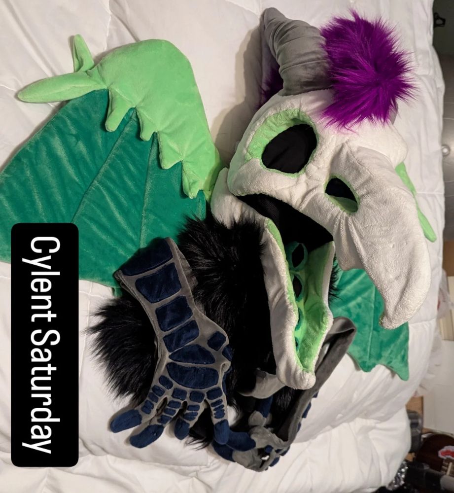 Partial fursuit of a skull crow-dragon with a purple hair tuft and green wings. Text on image: Cylent Saturday 