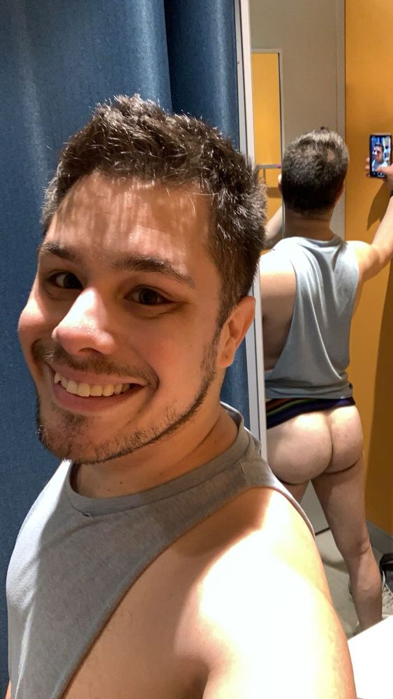 Young man with short hair taking a selfie. Behind him is a mirror, revealing mg he had no pants on and his booty is quite “cheeked up”