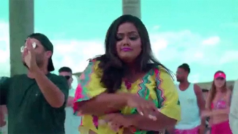 a woman in a colorful shirt is dancing with a group of people in a video .