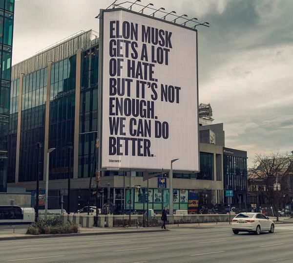 A big bulletin board at a city says: Elon Musk gets a lot of hate. but it's nog enough. We can do better.