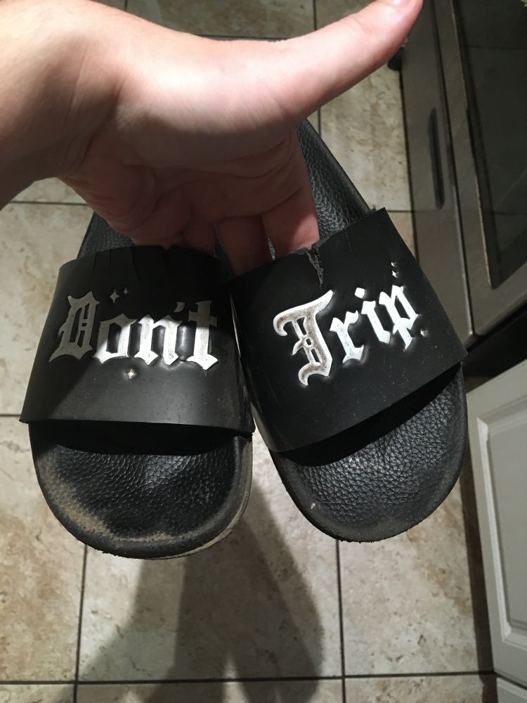 A battered pair of slides with “Don’t Trip” in blackletter type, one word on each strap of each slide. 