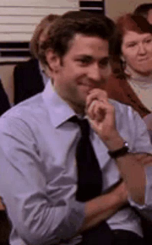 a man in a suit and tie is smiling while sitting in front of a crowd .