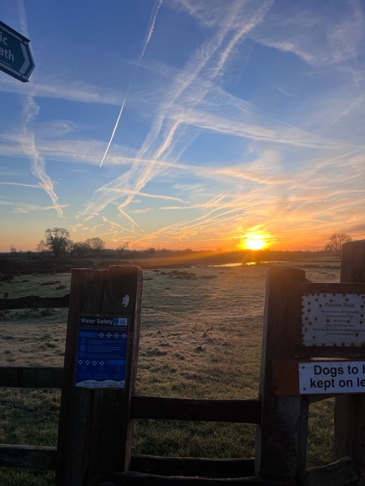 A wooden stile looking over a frosty field with a sunrise 