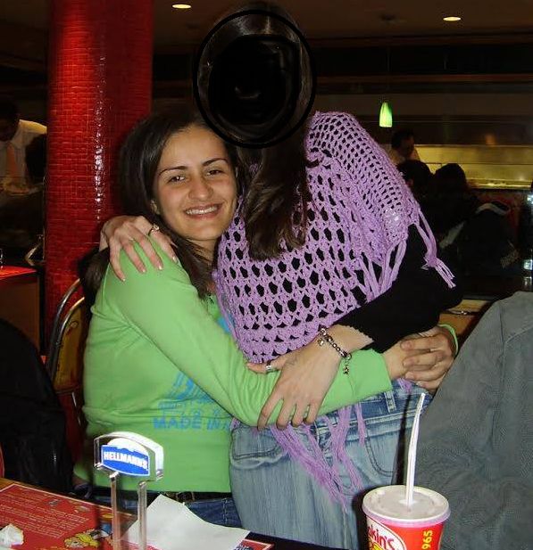 Eu aos 20 anos, mulher branca de cabelo e olhos castanhos, usando blusa verde de mangas longas, sentada numa lanchonete abraçada com uma amiga que está no meu colo - borrei a cara dela porque não falo com ela há anos, sei lá. 