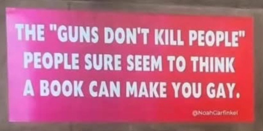 A red billboard with the words,”The ‘guns don’t kill people’ sure seem to think a book can make you gay.