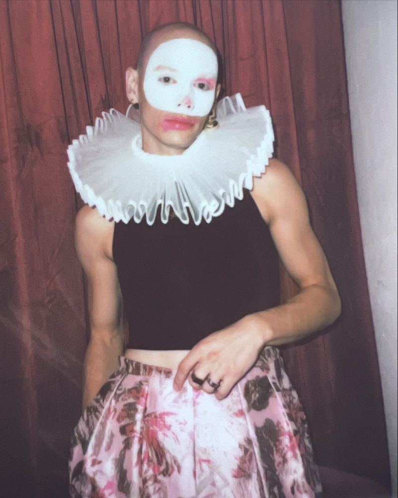 That gorl Bambi looks amazing standing in front of a red velvet curtain and wearing a crop top, pink silk pants, an Elizabethan collar, and (very chic) clown makeup. 