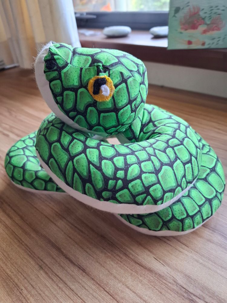 Vibrant green sewn snake with cream underbelly and yellow eyes. It is coiled up with head on top.