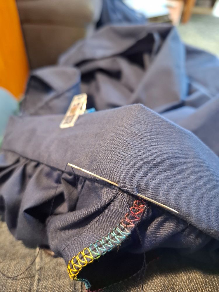 Needle in the waistband of some navy fabric with rainbow overlooking in the foreground.