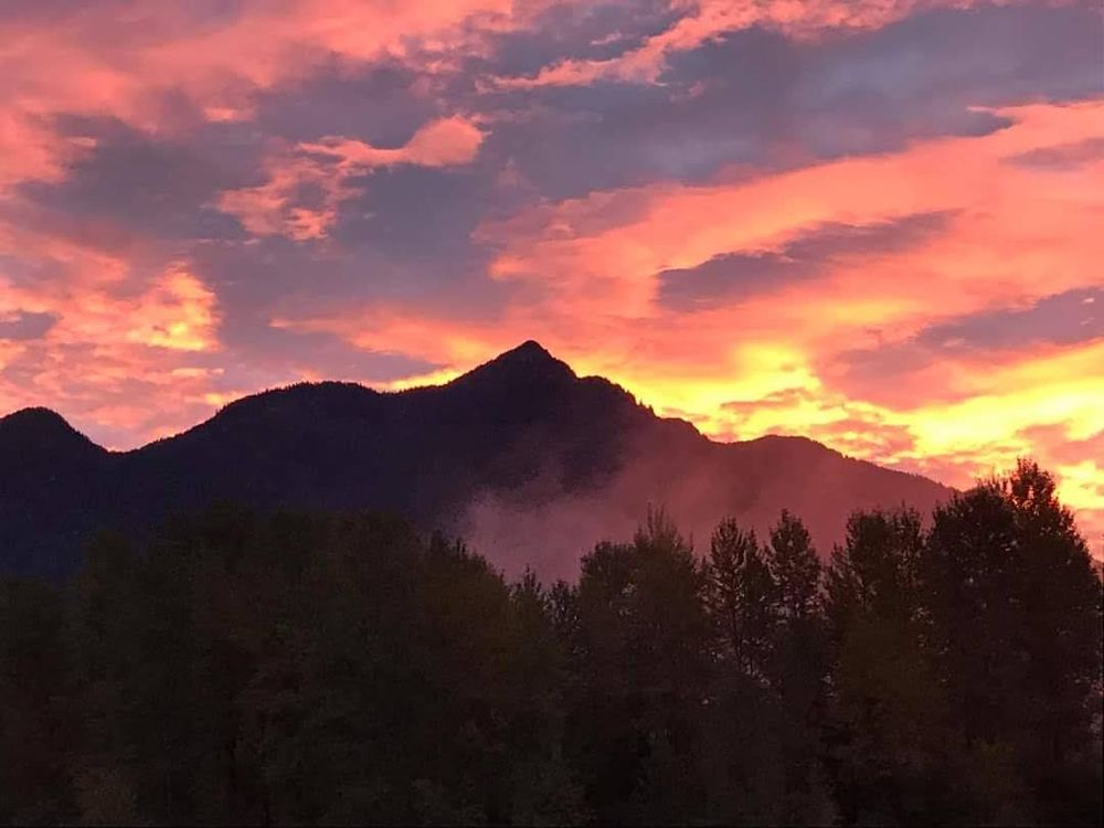 Sunrise over Mt. Ogilvie, Hope, BC, Canada. A blaze of gold behind the peak with orange and purple streaks above.