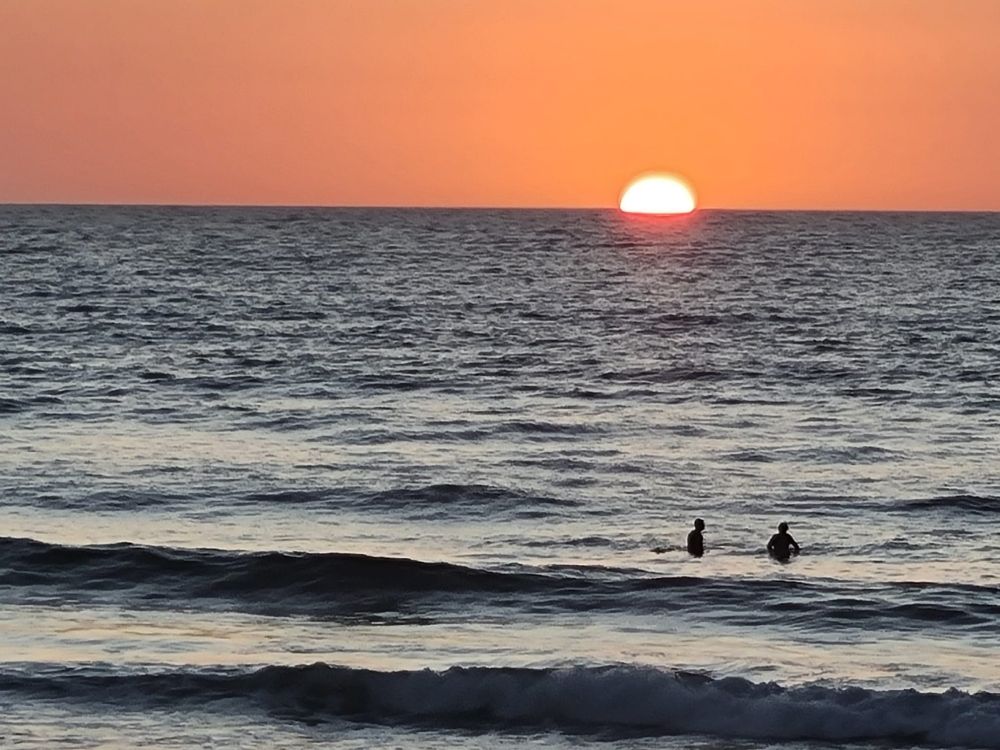 Sunset in west Africa. Two swimmers in the waves.