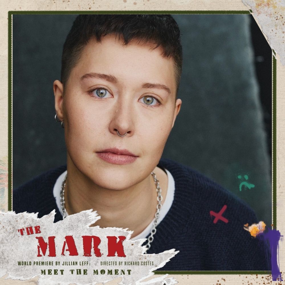 An androgynous person with short, dark hair and green eyes, smiling slightly and wearing a silver chain. 