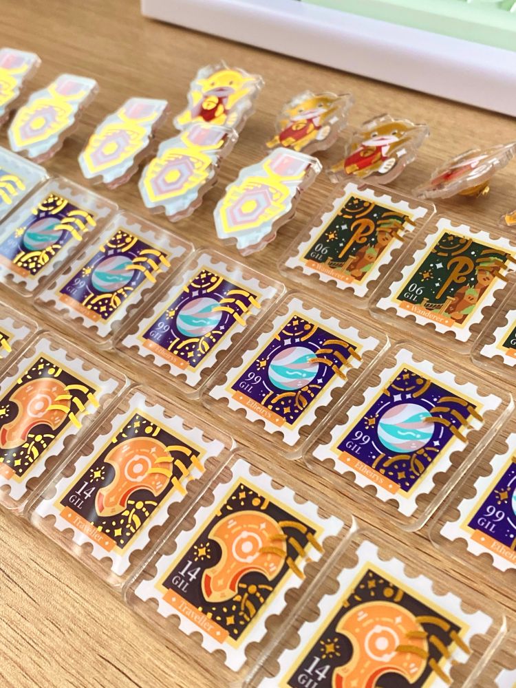 Rows of acrylic gold foiled stamp pins.
From top down
Namazu, Battle High 5, Oschon, Etheirys, Azem