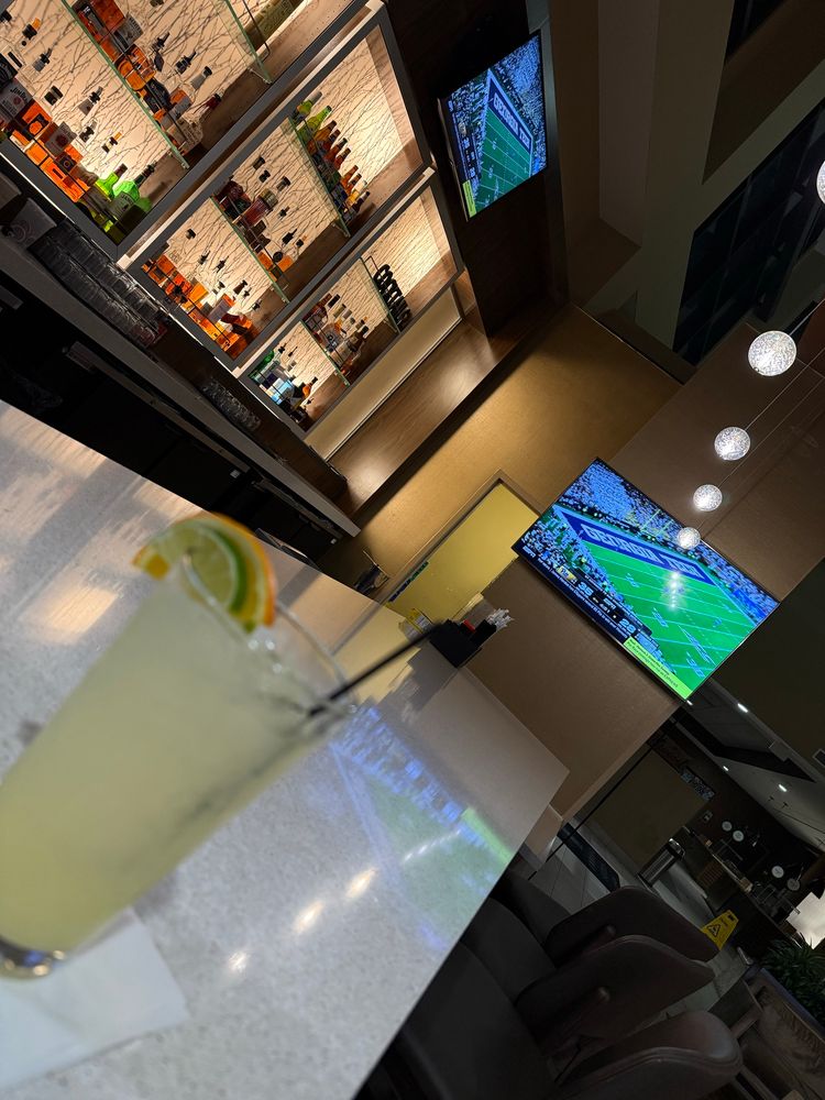 A margarita in a glass on the bar with the Pitt game on two TVs behind it 