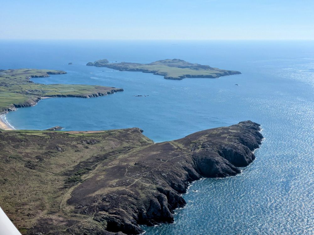 Aerial photo with long rocky headland in foreground & an island in the blue sea beyond 