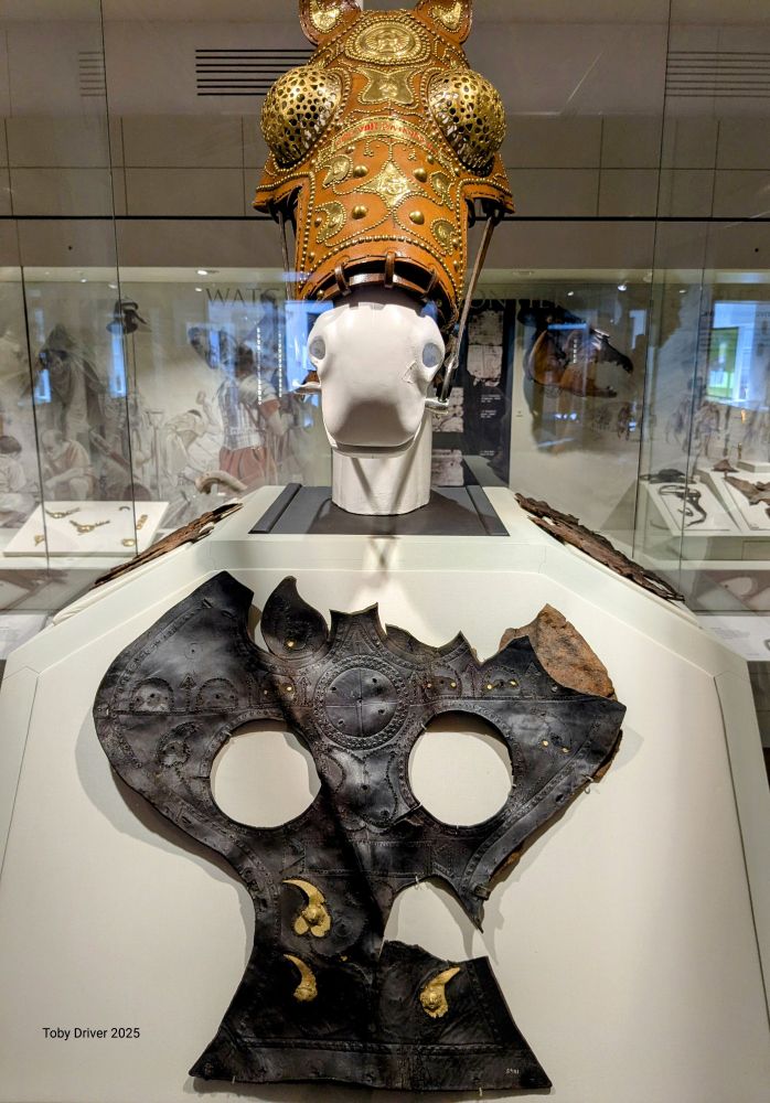 An original Roman leather horse mask in the foreground with a reconstructed horse head in the rear