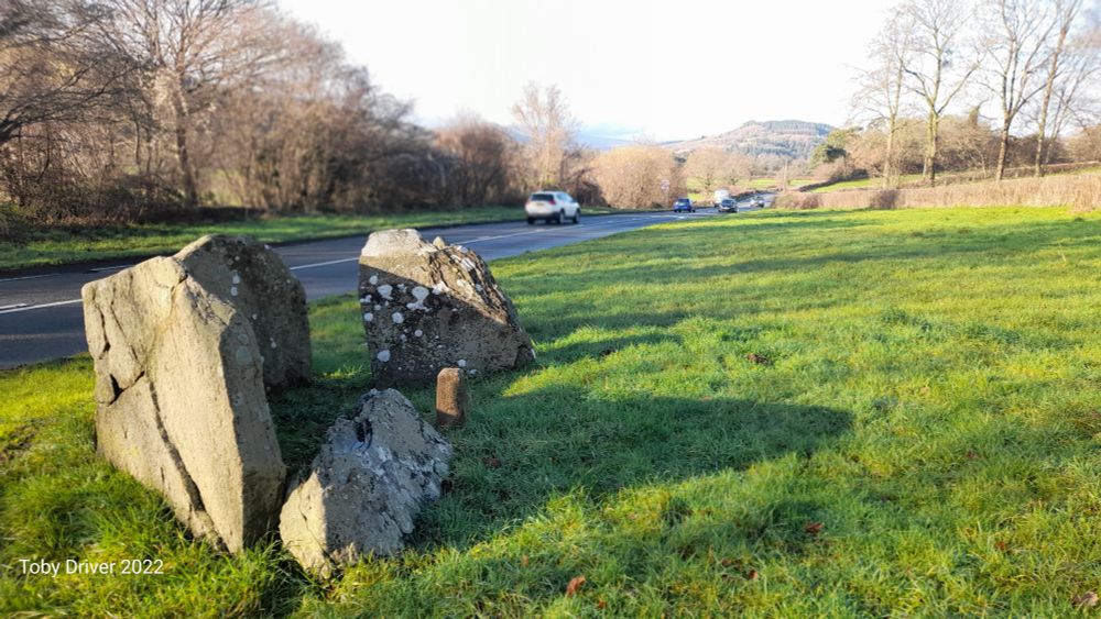 A stone slab chamber on a grassy verge with cars passing 