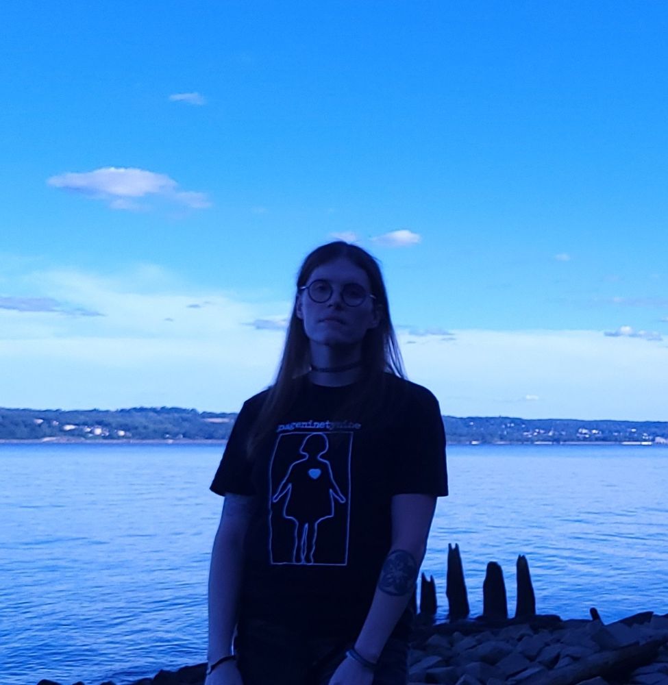 A blue-tinged picture of sheisinfinite in front of a large body of water.