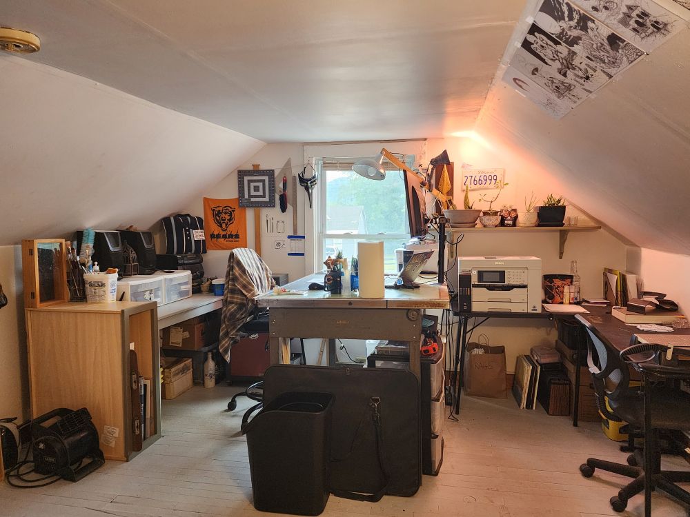An office with a drafting desk, shelving and various art studio stuffs.