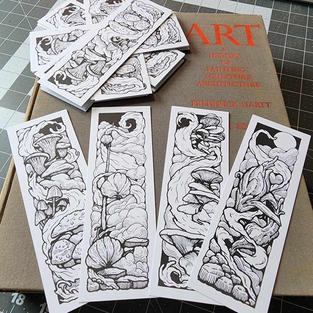 A pile of bookmarks featuring black and white botanical and fungi illustrations sitting on an art history book.