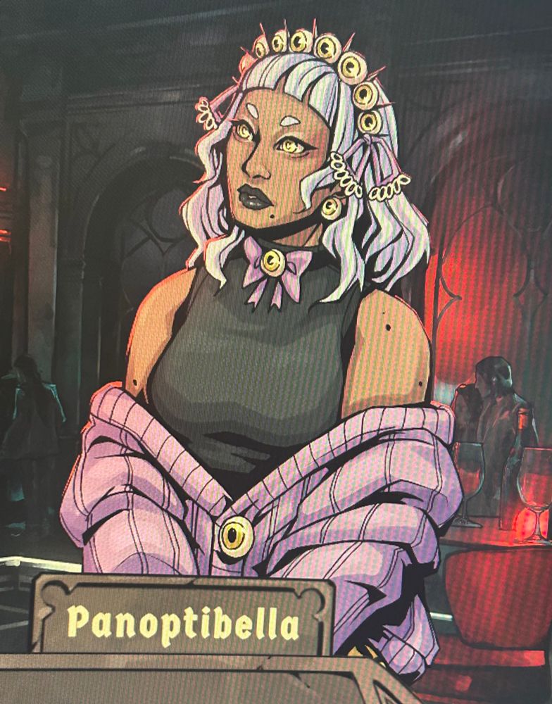 Character named Panoptibella from the game Vampire Therapist. She has brown skin, light blue hair with a headband of eyeballs, bright yellow eyes, black lipstick, eyeball earrings and bowtie, a black sleeveless top, and a purple cardigan with eyeball buttons