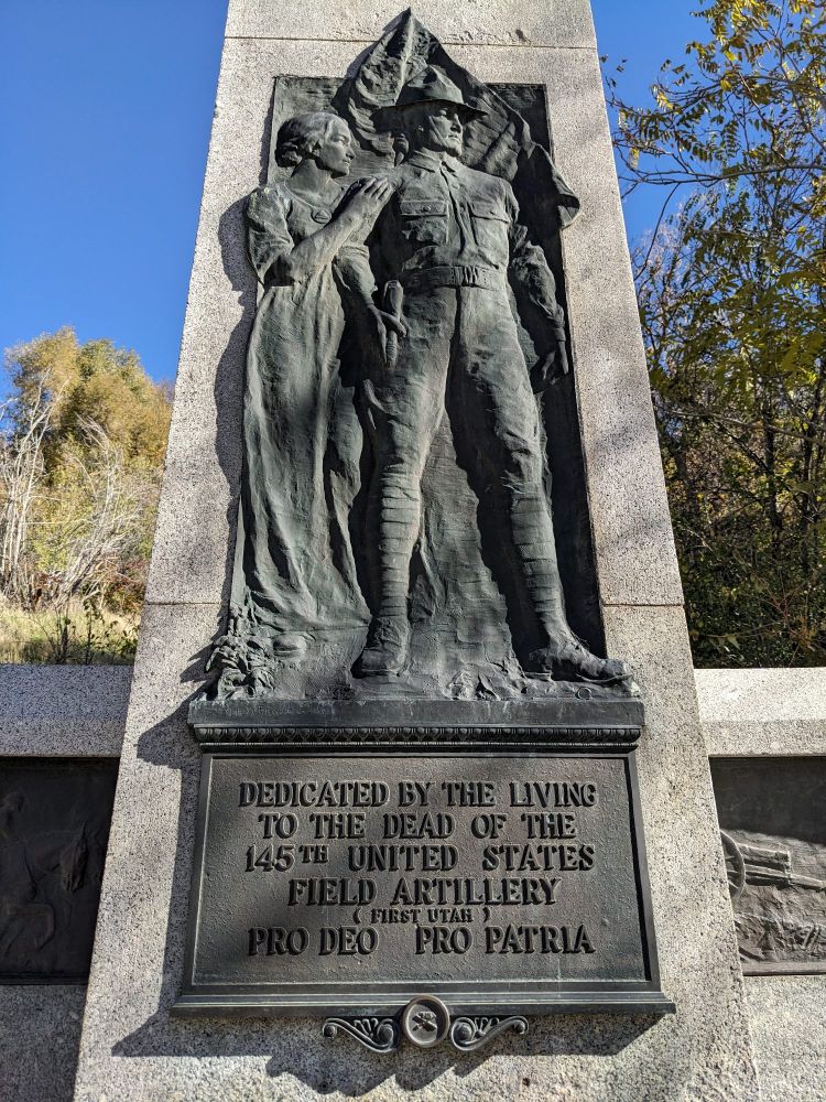 A bronze relief of a WWI doughboy and a woman at his back labeled "Dedicated by the living to the dead of the 145th United States Field Artillery (First Utah) Pro Deo Pro Patria."