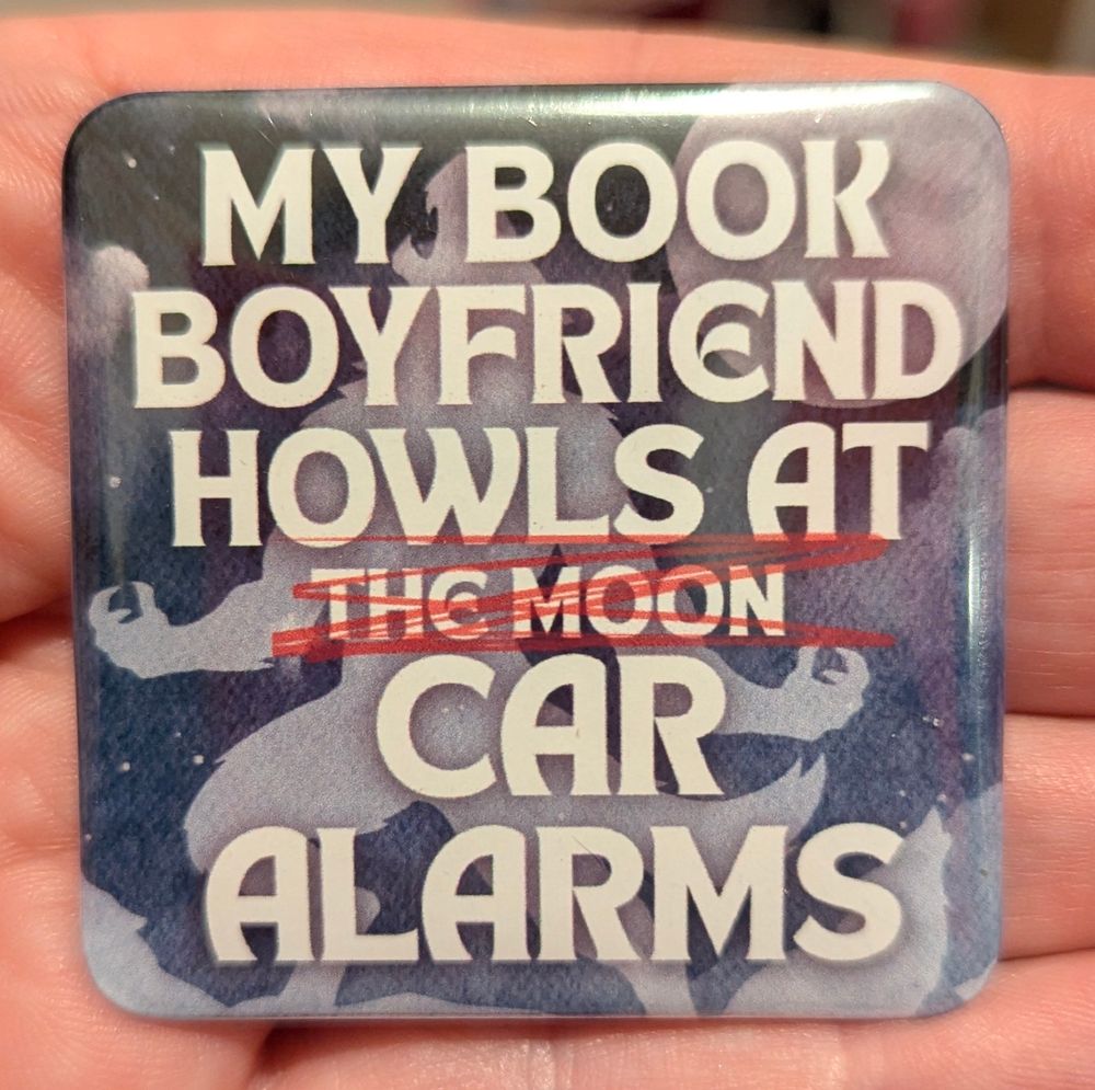 Big blue square badge with the silhouette of a werewolf and the moon in the background. Text reads "My Book Boyfriend Howls At [The Moon is crossed out] Car Alarms". 