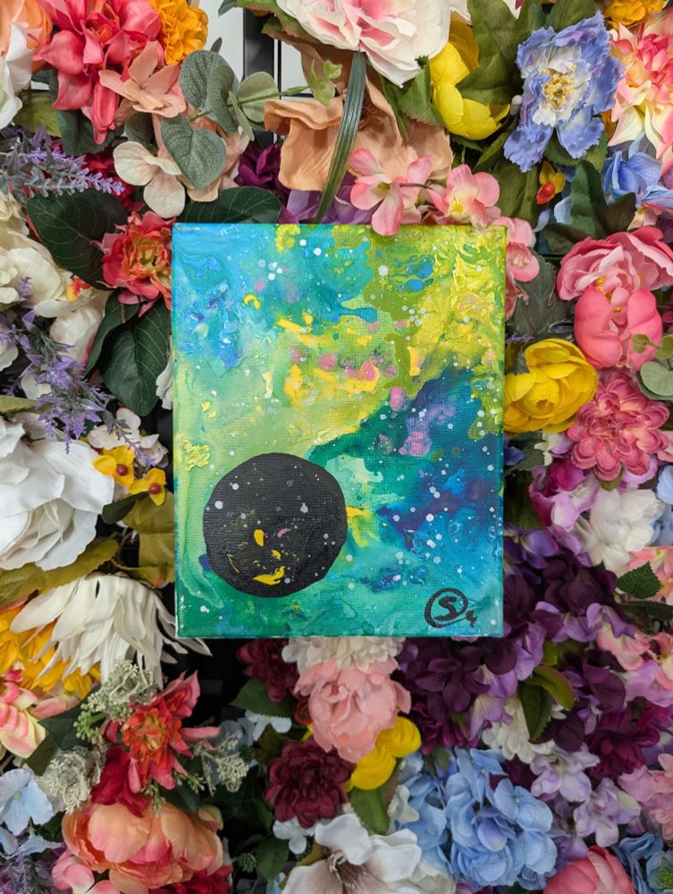 A painting on top of a background of colorful flowers.
The whole canvas is covered in a starry green, blue, and yellow nebula with spots of pink. A black planet hangs in the lower left corner.