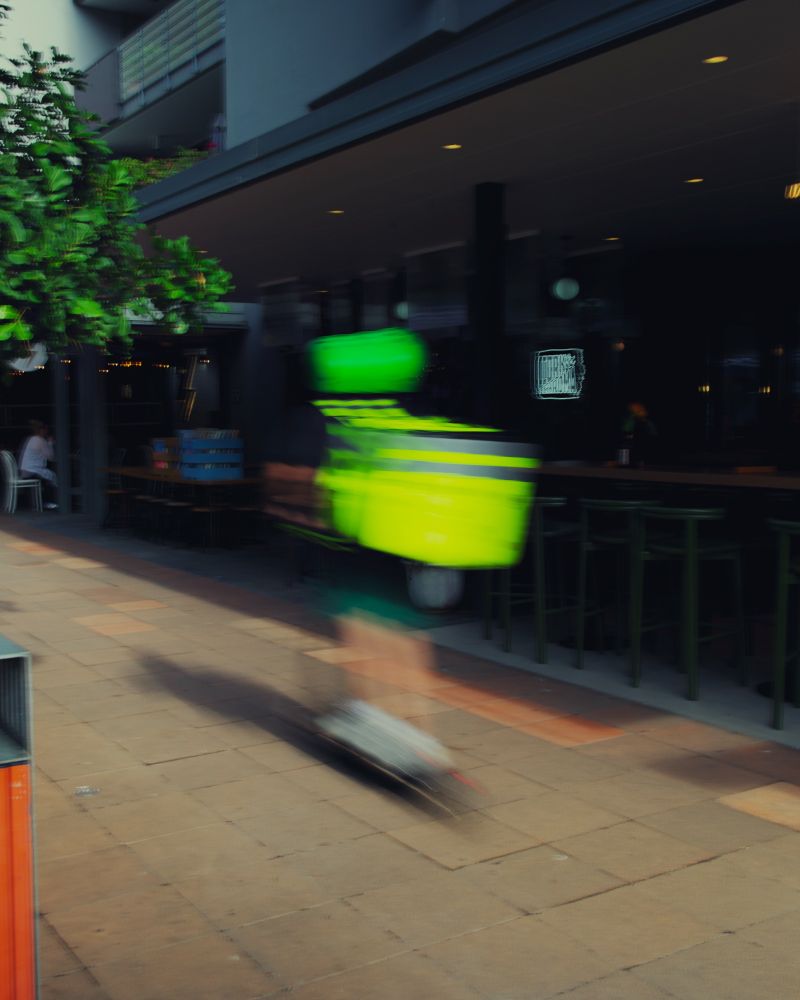 Fluoro green and yellow blurb of a food delivery person on an electric scooter. Not a technically great photo it was fun and from the hip